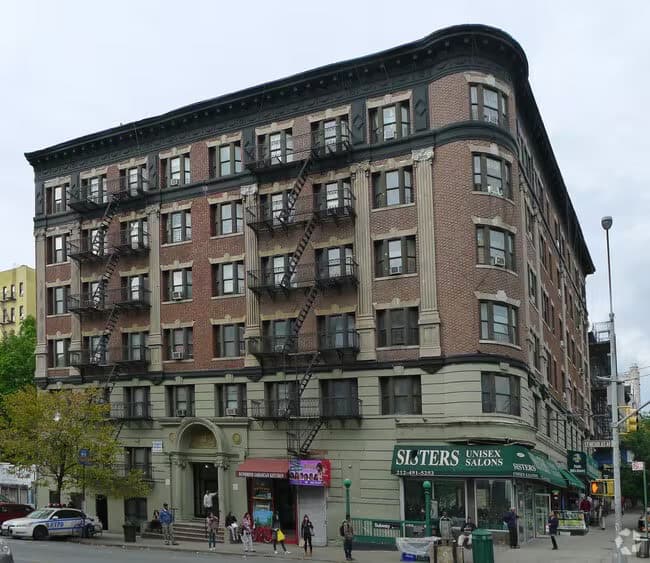Six-story mixed-use brick building in Harlem with ground-floor shops and a rounded corner