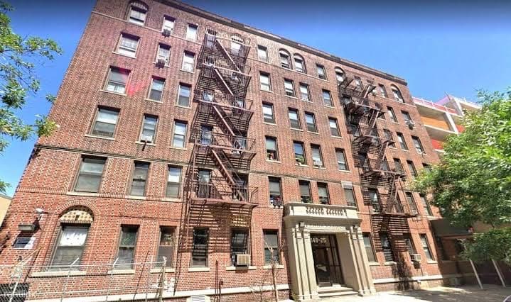 Six-story red-brick residential building with fire escapes and a stone entryway