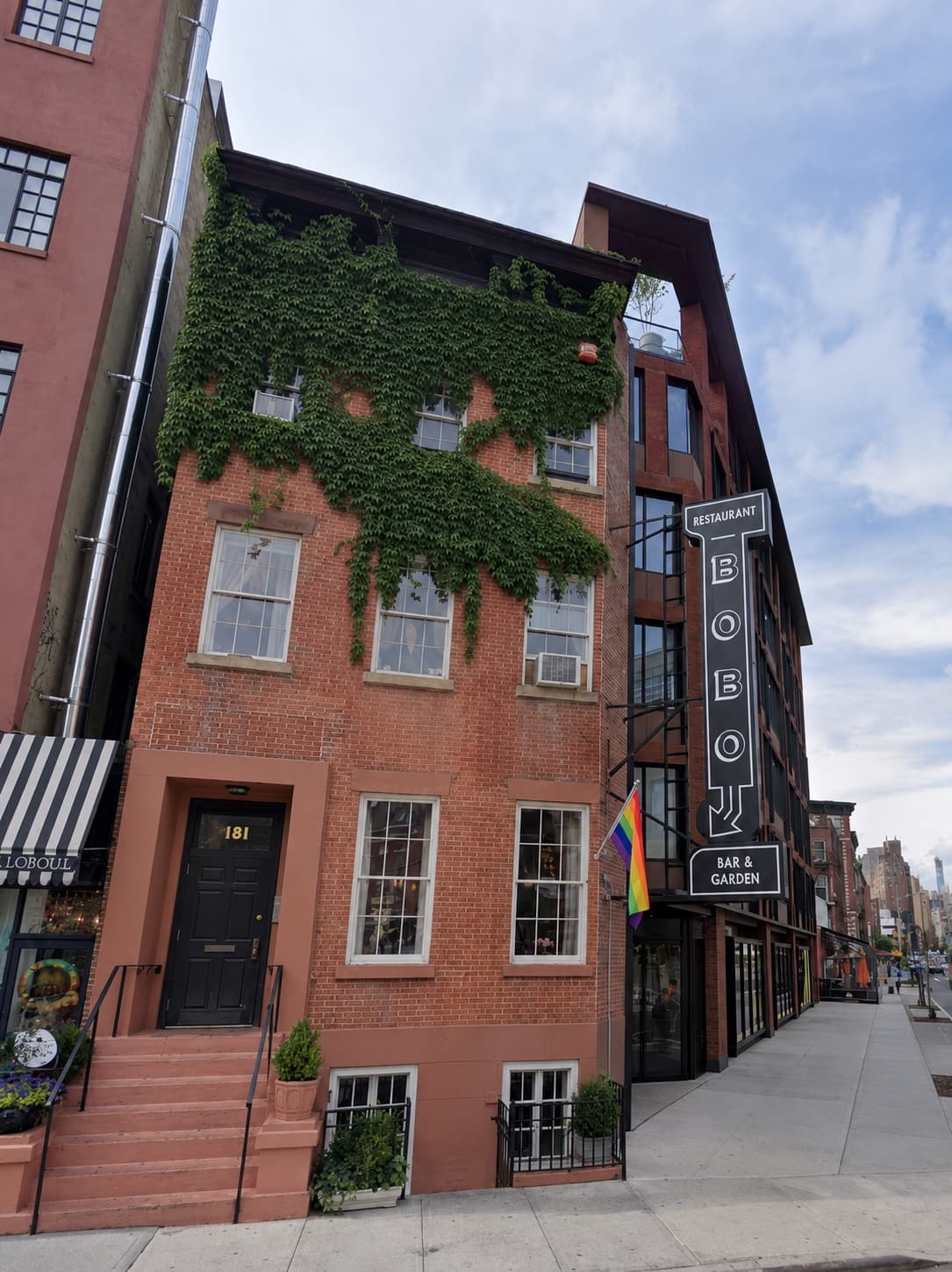 Four-story red brick mixed-use building in the West Village, ivy on the upper floors, entrance numbered 181, and a vertical sign for Bobo Restaurant, Bar & Garden